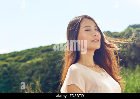 junge chinesische Schönheit in der Natur mit Wind geblasen Haar Lächeln Stockfoto