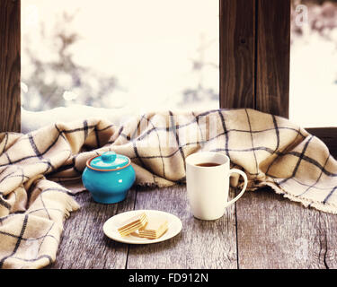 Weiße Tasse Kaffee oder Tee, blauen Topf und wollene Plaid befindet sich auf stilisierte hölzerne Fensterbank. Winter-Konzept von Komfort und rela Stockfoto