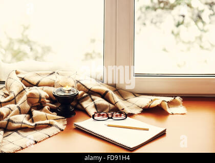 Öffnen Sie Notepad, Brille, Kerze, Bleistift und Beige warmen Plaid befindet sich auf stilisierte hölzerne Fensterbank. Winter-Konzept von Komfort und Stockfoto