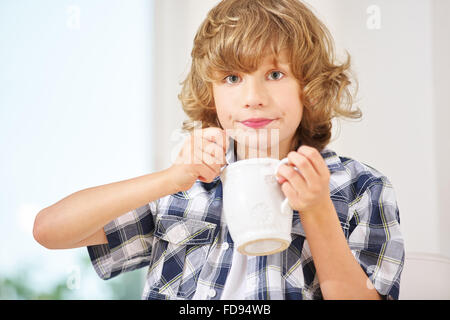 Fröhlicher Junge, Essen und trinken aus einer Tasse heißer Schokolade Stockfoto