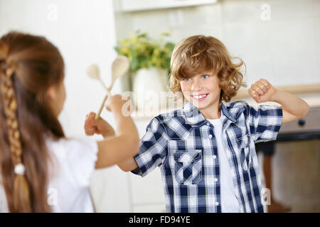 Zwei Kinder kämpfen im Scherz in der Küche mit Holzlöffel Stockfoto