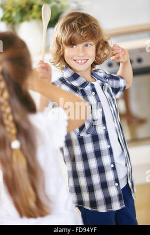 Jungen und Mädchen kämpfen in Scherz mit Holzlöffel in einer Küche Stockfoto