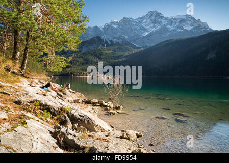 Zwei Frauen Sonnenbad am See Eibsee, bedeckt Schnee Wettersteingebirge und herbstliche Wälder, Garmisch-Partenkirchen, Deutschland Stockfoto