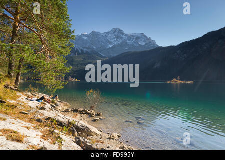 Zwei Frauen Sonnenbad am See Eibsee, bedeckt Schnee Wettersteingebirge und herbstliche Wälder, Garmisch-Partenkirchen, Deutschland Stockfoto