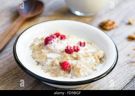 Haferflocken-Porridge mit Himbeeren und Milch auf strukturierte Holztisch, gesundes Frühstück im Land Stil, selektiven Fokus Stockfoto