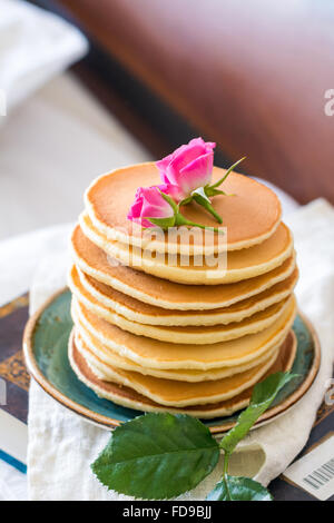 Stapel von Pfannkuchen und Rosenblüten ans Bett serviert Stockfoto