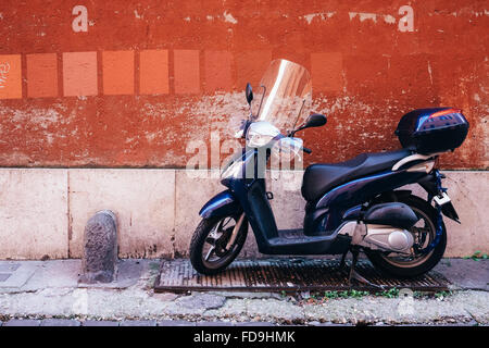 Orange Farbe Farbfelder auf einem abgenutzten roten Wand in Rom, Italien, mit einem Roller unter geparkt Stockfoto