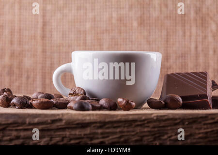 Tasse, Kaffee-Bohnen, Schokolade auf einem Holzbrett Closeup Hintergrund Stockfoto