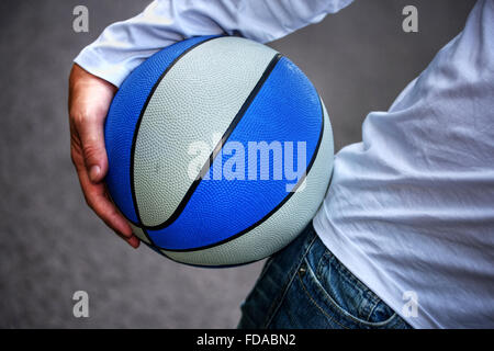 Mann in weißer Oberseite hält einen Basketball unterm Arm. Stockfoto