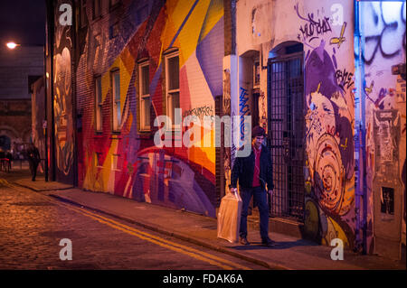 Junger Mann in der Nacht zu Fuß vorbei an Straßenkunst im trendigen Shoreditch, East London Stockfoto