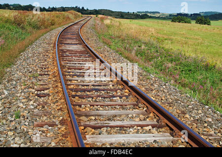 Rostige Gleise auf einem Bahndamm zwischen Wiesen, Hügeln im Hintergrund Stockfoto