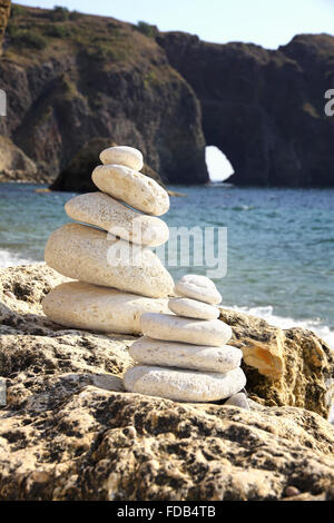 Stapel von Steinen am Strand mit Dianas Grotte auf einem Hintergrund. Krim, Schwarzes Meer, Ukraine Stockfoto