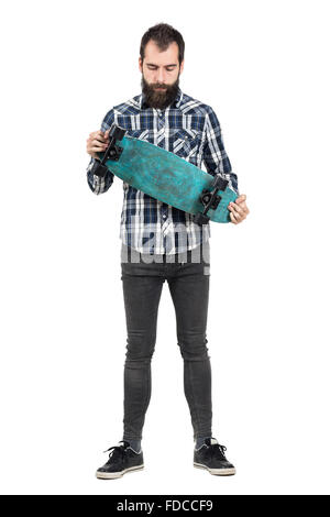 Junge Hipster in Tartan Shirt Skateboard auf der Suche nach unten halten. Ganzkörper-Länge-Porträt über weiße Studio-Hintergrund isoliert Stockfoto