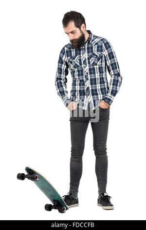 Bärtige Hipster auf Skate Longboard mit Händen in der Tasche nach unten stehen. Ganzkörper-Länge-Porträt über weißen isoliert Stockfoto