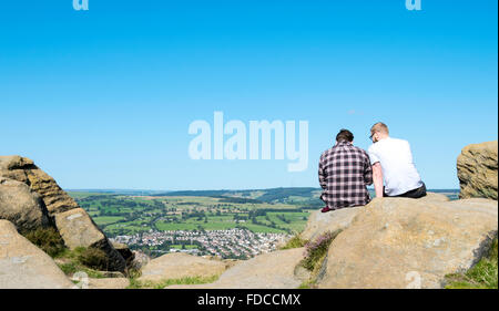 Zwei Menschen sitzen auf einem Sandstein Felsen mit Blick auf Otley Chevin Waldpark in West Yorkshire, Großbritannien. Stockfoto