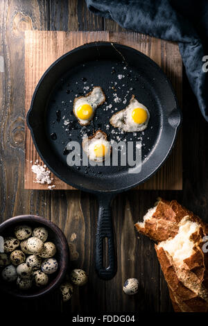 Wachtel-Spiegeleier in einer gusseisernen Pfanne mit knusprigem Brot Stockfoto