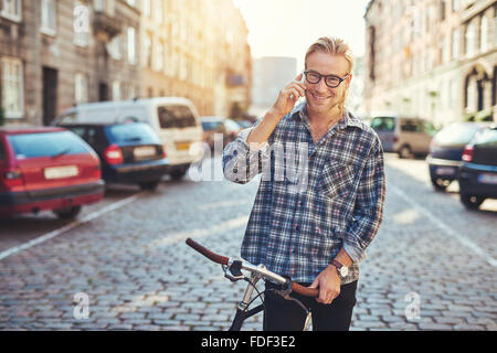 Glücklich Jüngling in der Stadt, geht auf sein Handy während lächelnd Stockfoto