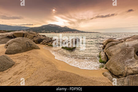 Dramatische Stimmungsvoller Himmel über Algajola Strand in Korsika mit Steinen und Sand im Vordergrund und das Dorf im Hintergrund Stockfoto