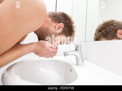 Mann trinkt Wasser aus dem Waschbecken Stockfoto