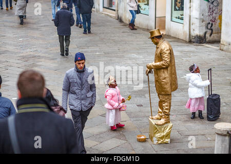 kleines Mädchen mit Interesse beobachten eine Straßenkünstler Verkleidung in goldene Statue in Venedig Italien Stockfoto