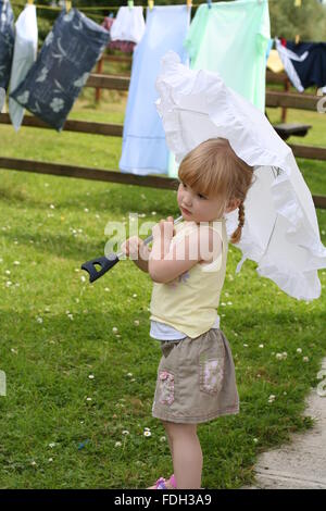 Kleine blonde Mädchen spielen im Garten im Sommer mal mit Zöpfen Pigtails im Haar ihrem Schirm Holding im Sommer Dublin Irland, Stockfoto