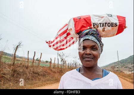 Frau ein Sack Kartoffeln auf dem Kopf auf einem Feldweg in der Hhohho Region von Swasiland, Afrika. Stockfoto