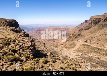 Zwei Menschen sitzen am Rand einer Klippe mit Blick auf die Berge in Lesotho, Afrika Stockfoto