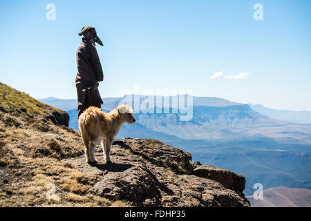 Hirte und sein Hund stand vor einer Bergkette eingewickelt in Decken in Lesotho, Afrika Stockfoto