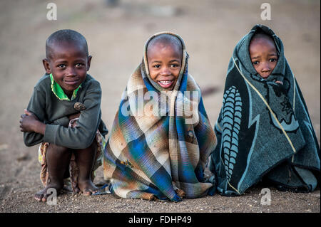 Drei junge Burschen in Decken gehüllt und sitzt auf den Schmutz Boden in Lesotho, Afrika Stockfoto