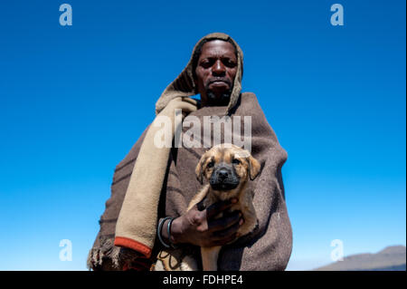 Hirte stehend in einer weiten Ebene, eingewickelt in decken halten einen Welpen in Lesotho, Afrika Stockfoto