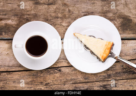 Ansicht von oben Bild der Tasse schwarzen Kaffee mit Stück Käsekuchen auf Holztisch. Frühstück-Menü-Hintergrund Stockfoto