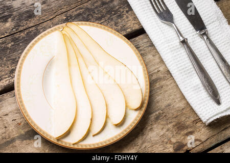 In Scheiben geschnitten reifen Birne auf Untertasse mit Besteck auf Holztisch. Draufsicht Dessert Obst Bild Gourmet-Menü-Hintergrund Stockfoto