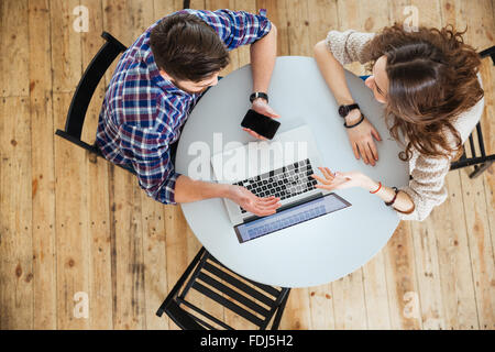 Draufsicht der schöne junge Paar sprechen, mit Laptop und halten leerer Bildschirm Handy am runden Tisch im café Stockfoto