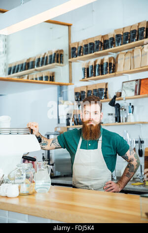 Bärtige Barista in weißer Schürze mit tätowierten Händen in Coffee-shop Stockfoto