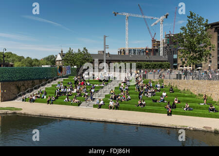 Menschenmenge genießen sonnige Nachmittag sitzen auf Kunstrasen durch Regents Canal, Kings Cross, London, UK Stockfoto