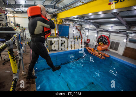 Ein Offshore-Arbeiter springt 3 Meter in ein Becken im Meer Überlebenstraining. Stockfoto