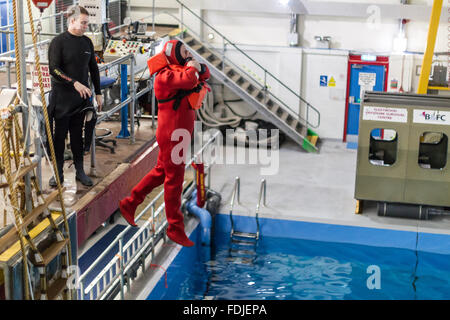 Ein Offshore-Arbeiter tragen einen Überlebensanzug springt 3 Meter in ein Becken im Meer Überlebenstraining. Stockfoto