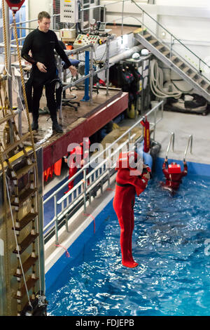 Ein Offshore-Arbeiter tragen einen Überlebensanzug springt 3 Meter in ein Becken im Meer Überlebenstraining. Stockfoto