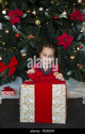 Lächelndes Mädchen sitzen Weihnachtsbaum Geschenk öffnen Stockfoto