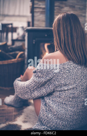 Rückansicht einer Frau sitzt vor einem Holzofen Stockfoto