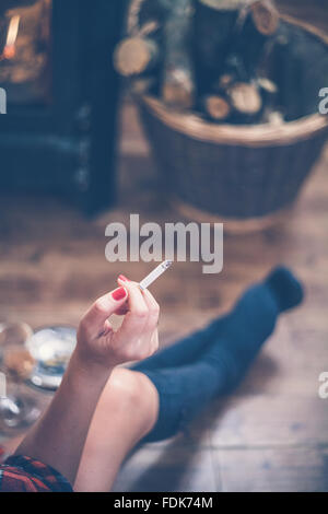 Frau sitzt vor Holzofen, eine Zigarette rauchend Stockfoto