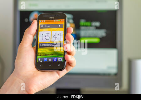 Hand hält ein HTC ein SV-Funktionen ein 4,3-Zoll-WVGA-Super-LCD2-Display vor Computer-Monitor. Stockfoto