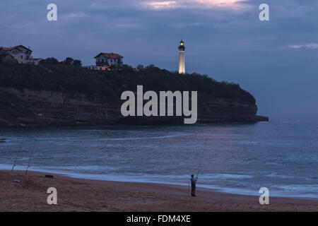 Ein Fischer im Chambre d ' Amour Strand von Twilight, mit Biarritz Leuchtturm im Hintergrund. Anglet, Aquitaine, Frankreich. Stockfoto