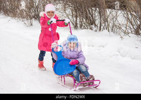 Zwei Mädchen Freundinnen fahren einander auf einem Schlitten in den schneereichen Winterwetter Stockfoto