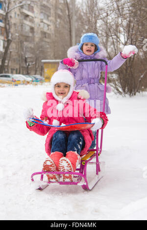 Zwei Mädchen Freundinnen fahren einander auf einem Schlitten in den schneereichen Winterwetter Stockfoto