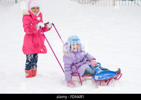 Zwei Mädchen Freundinnen fahren einander auf einem Schlitten in den schneereichen Winterwetter Stockfoto