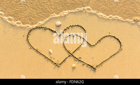 Zwei Herzen auf der Sandstrand mit der weichen Welle gezogen. Flitterwochen-Konzept. Stockfoto