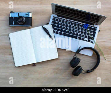 Laptop, Kamera, Kopfhörer und ein Notebook mit einem Stift auf einem Holztisch gelegt. Stockfoto