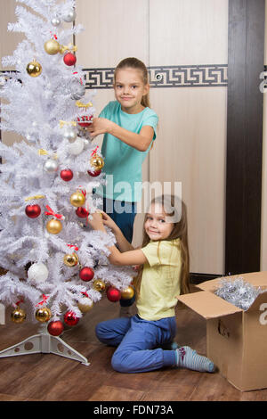 Lustiges Mädchen entfernen Weihnachtsschmuck mit künstlicher Weihnachtsbaum Stockfoto