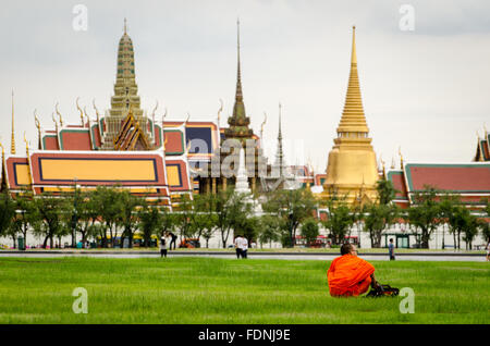 Bangkok, buddhistisch Mönch sitzt in Sanam Luang Park mit Wat Phra Kaeo im Hintergrund Stockfoto